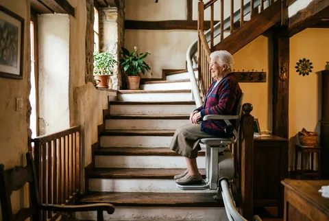 Persona mayor en una silla salvaescaleras subiendo una escalera de casa