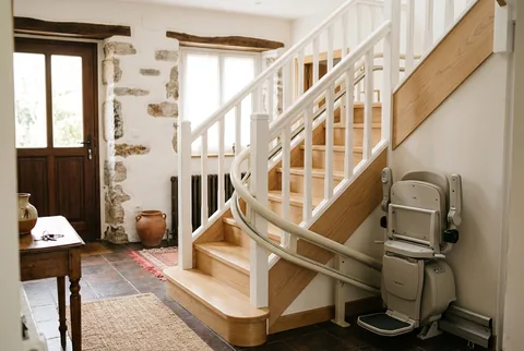 Silla salvaescaleras plegada con raíl curvo en una escalera de madera blanca